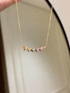 Détail d'un collier doré doté d'un pendentif en zircon coloré avec un design de barre courbe.