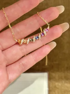 Gros plan d'un collier en or avec un pendentif incurvé serti de zircons multicolores.