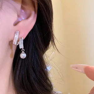 Silver needle earrings with sparkling zircons and a white round pearl drop on ear.
