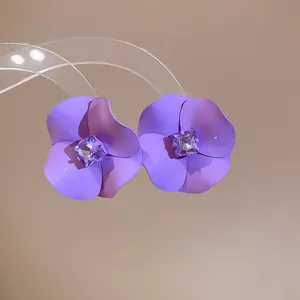 Detailed close-up of purple matte flower stud earrings with a sparkling central square crystal