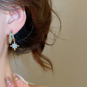 Macro view of elegant gold hoop earrings with a sparkling blue zircon star charm.