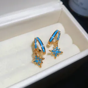 Close-up of gold-plated star earrings with turquoise blue stone inlays in a white box