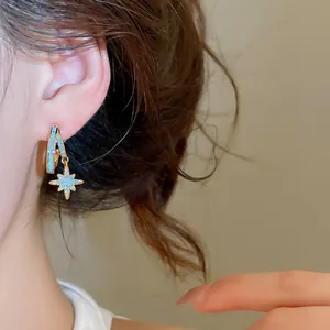Detail view of elegant gold starburst hoop earrings with blue zircon stones on model's ear