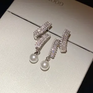 Close-up of elegant silver needle earrings with shimmering zircons and dangling pearls