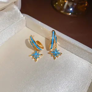 Macro detail of gold-tone star dangle earrings with turquoise stones in a box