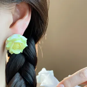 Close-up of a sweet light green resin rose stud earring on an ear with braided hair