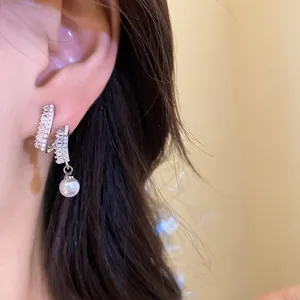 Detail shot of elegant silver needle earrings featuring zircon inlay and a lustrous round pearl