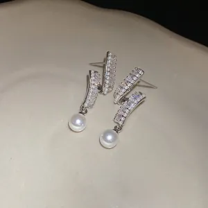 Close-up of elegant silver stud earrings with sparkling zircons and white pearl drops