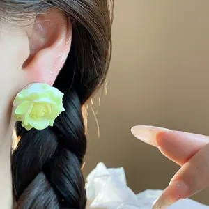 Detailed shot of a pale green resin rose flower stud earring worn on a model's ear