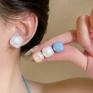 Detailed close-up showing white and blue minimalist geometric pearl stud earrings on ear