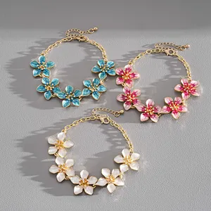 Detailed view of three enamel flower bracelets in blue, pink, and white with gold chains.