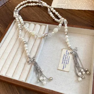 Elegant long beaded necklace featuring white pearls and rhinestone-encrusted bow tassels in a box