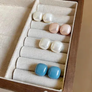 Detailed macro view of colorful geometric pearly stud earrings in a wooden jewelry box