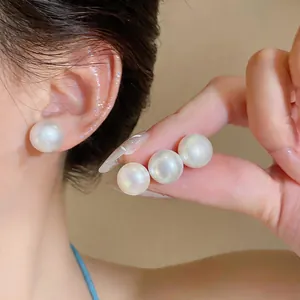 Close-up detail of elegant white pearl stud earrings showing luster and size on an ear.