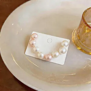 Close-up of U-shaped pearl earrings featuring white and pink pearls on display card