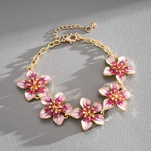 Close-up detail of a gold-tone metal bracelet with five pink and white enamel flowers
