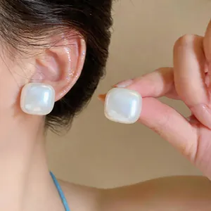 Close-up showing the elegant luster of large square pearlescent stud earrings on ear.