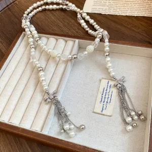 Detailed view of long pearl necklace featuring rhinestone bows and chain tassels.