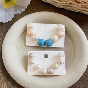 Detailed view of minimalist geometric and round pearl stud earrings on white cards
