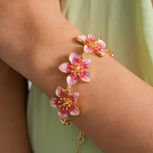 Close-up view of a stylish gold-tone bracelet featuring pink enamel flower charms on wrist.
