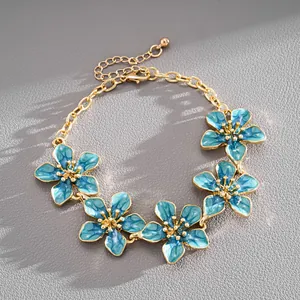 Detail shot of an elegant gold-tone metal bracelet featuring blue enamel flowers