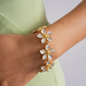 Close-up of a delicate gold-toned bracelet with white enamel flowers on a female wrist.