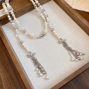 Detailed macro view of a long pearl necklace with rhinestone bow tassels in a wooden tray.