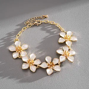 Detailed view of gold chain bracelet with five white enamel flower charms on grey leather