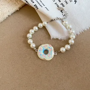Gros plan d'un bracelet en perles de style crème avec un pendentif donut coloré.