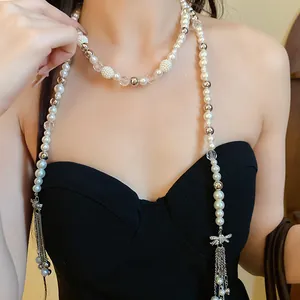 Close-up of long pearl necklace with rhinestone bow charm and chain tassels