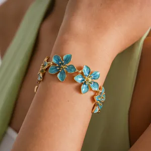 Detail view of a gold-toned bracelet featuring blue enameled flower charms on a wrist.