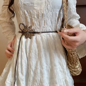 Detail des ethnischen handgeflochtenen Gürtels mit Blumenschnalle auf weißem Spitzenkleid