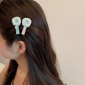 Détail de barrettes beignet avec breloques en strass portées sur cheveux foncés.