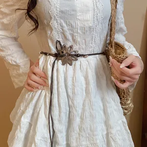 Detailansicht eines braunen handgeflochtenen Gürtels mit Holzblume auf weißem Kleid