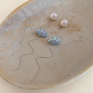 Dettaglio ravvicinato di orecchini a nappa con nuvola iridescente e perle su piatto