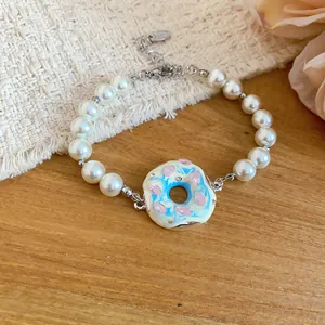 Vue détaillée d'une breloque donut et de perles blanches sur un bracelet de style doux.