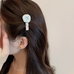 Détail d'une pince à cheveux beignet à la crème sur cheveux bruns avec collier perles