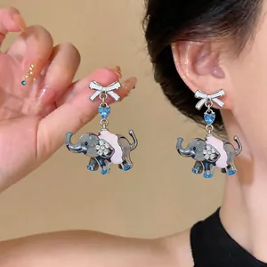 Detail shot of cute cartoon elephant earrings with white bow and blue heart zircon.