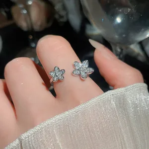 Close-up detail of a minimalist silver open ring with sparkling flower zircons on finger