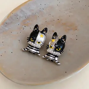 Asymmetric black and silver cat stud earrings featuring yellow star and pearl detail