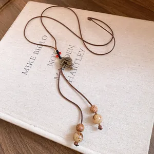 Gros plan d'un collier ethnique avec pendentif feuille et cordon tressé sur un livre.