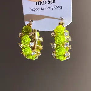 Detailansicht der leuchtend grünen Harzrosen und funkelnden Strasssteine auf goldenen Ohrringen