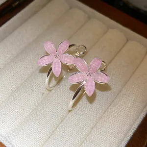 Detalle de pendientes de aro con flores de resina rosa y aguja de plata en estuche de lujo.