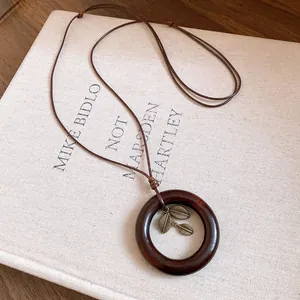 Détail d'un long collier tissé à la main avec pendentif anneau bois et breloque feuille.