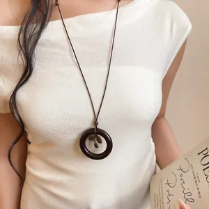 Vue détaillée d'un collier pendentif vintage en bois rond avec breloque feuille sur blanc