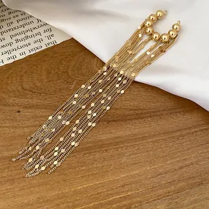 Detailansicht eleganter langer goldener Quasten-Ohrclips auf einer natürlichen Holzoberfläche