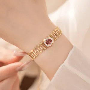 Primer plano de una pulsera calada de oro con circonita roja central en muñeca femenina.