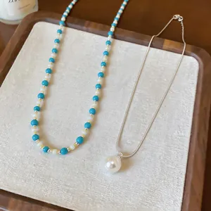 Primo piano di una collana di perle turchesi e una catena d'argento con pendente di perla.