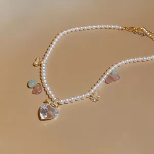Detailed view of pearl necklace with a large clear heart zircon and dainty butterfly charms