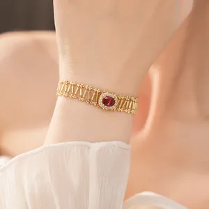 Primer plano de una pulsera dorada vintage con circonita roja central ovalada en mano.